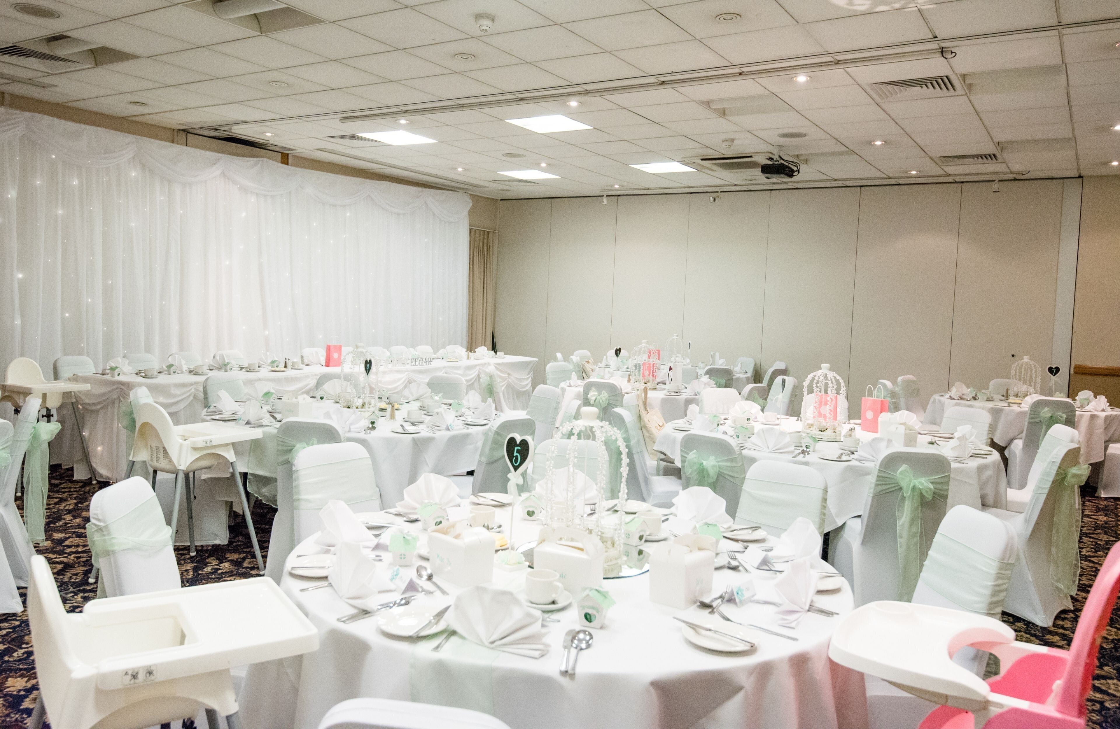 A banquet hall with round tables, white tablecloths, and chairs with green sashes.