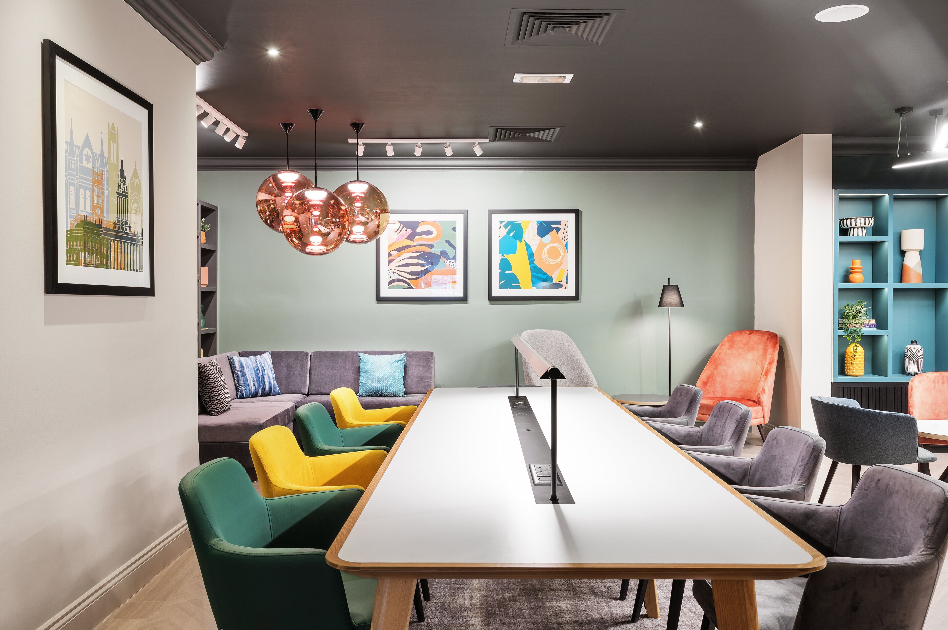 A modern meeting room with a long table, colorful chairs, a sofa, and abstract art on the walls.