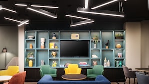 A modern lounge area with a large flat-screen TV, colorful chairs, and a variety of decorative items on shelves. - Holiday Inn Leeds Wakefield M1 Jct.40 by IHG (Ossett)