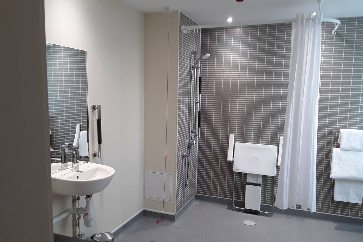 A modern bathroom with a sink, mirror, shower, and towel rack.