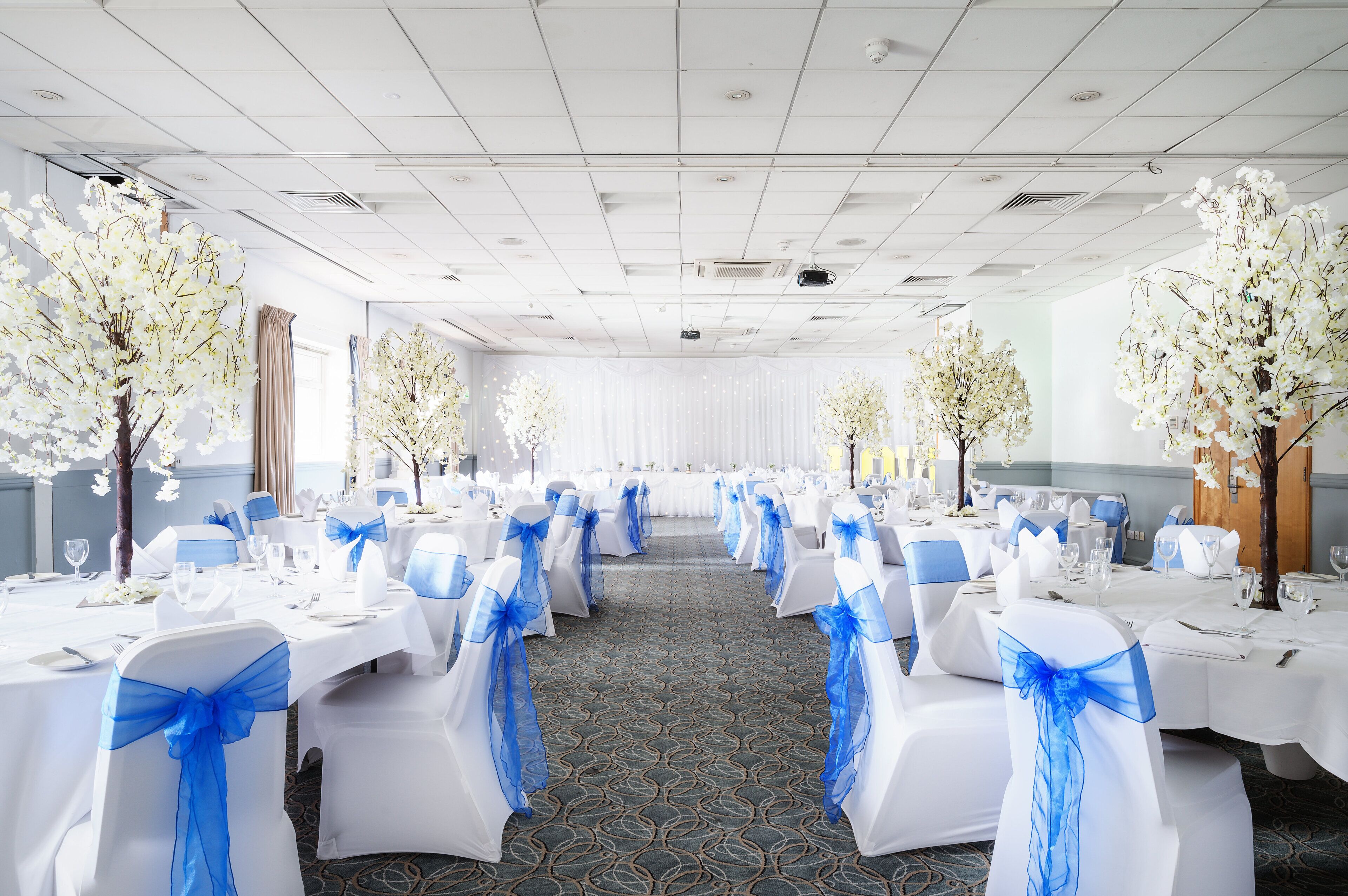 A banquet hall with tables set for a formal event, featuring white tablecloths and blue sashes.