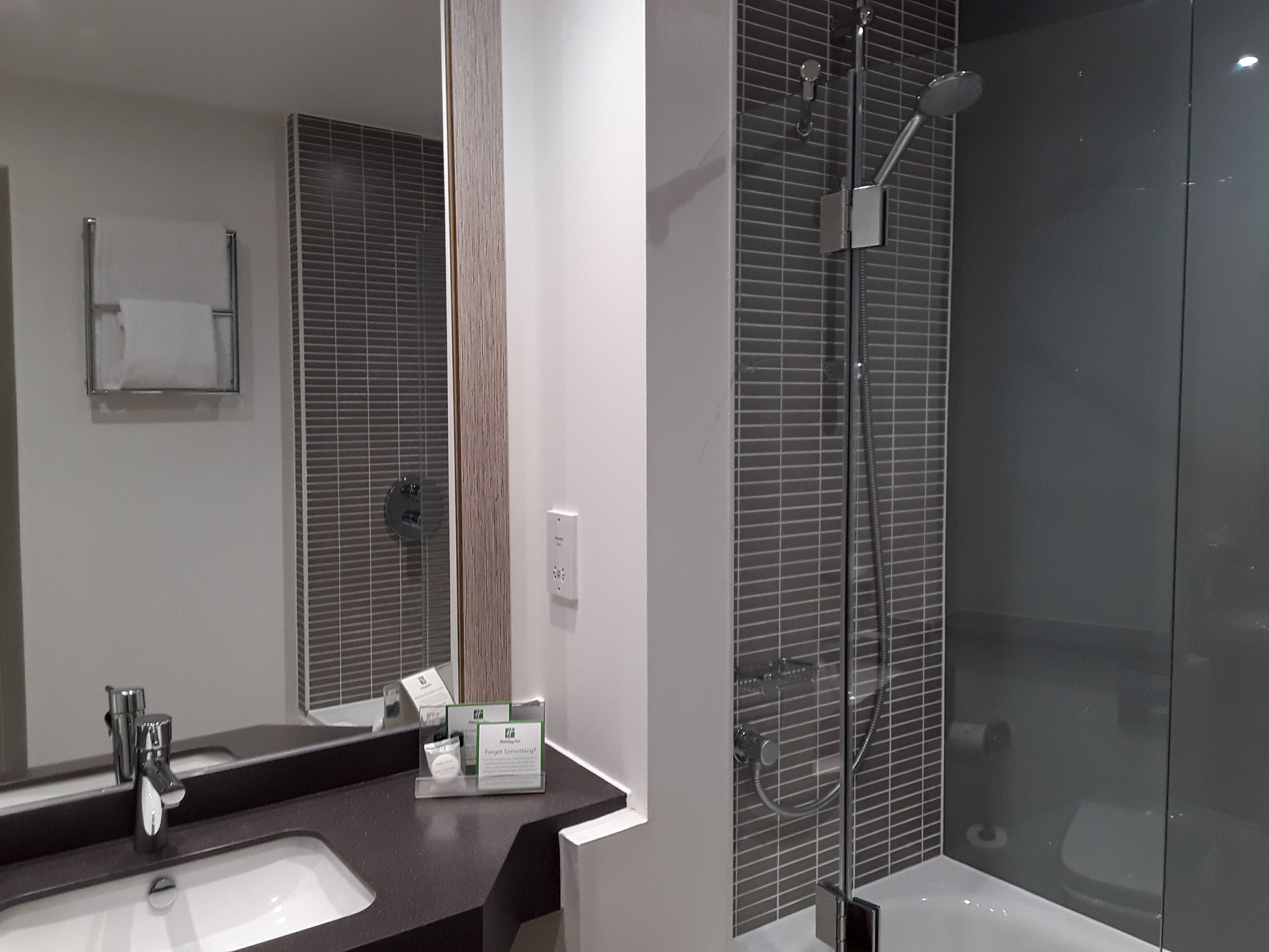Un baño moderno con un espejo grande, un lavamanos, una ducha con puerta de cristal y un perchero para toallas.