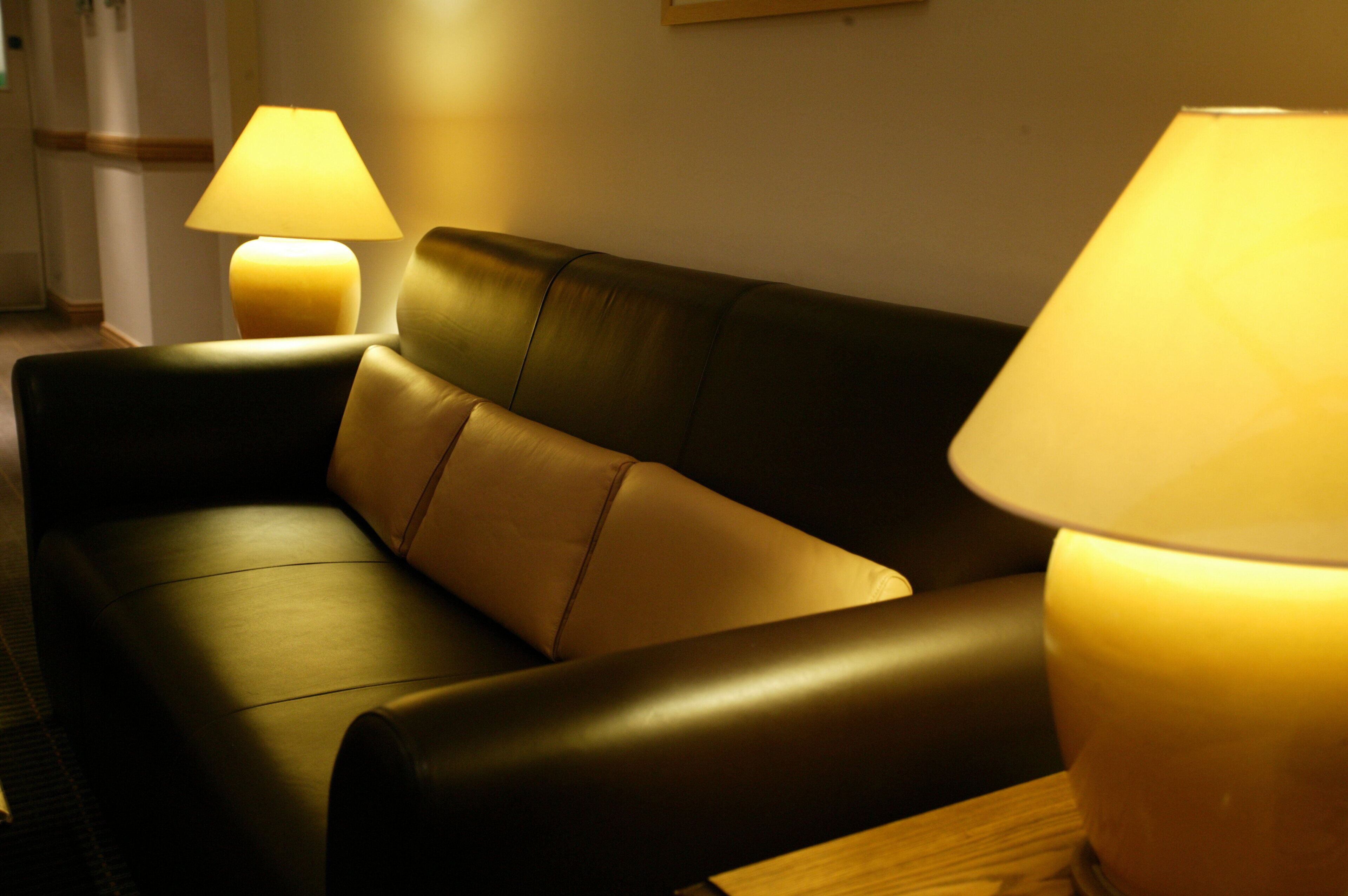 A dark leather sofa with a light-colored cushion, accompanied by two table lamps with lampshades.