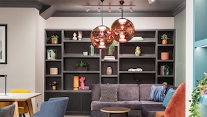 A modern living room with a grey sofa, blue chairs, a round wooden coffee table, and a bookshelf filled with decorative items. - Holiday Inn Leeds Wakefield M1 Jct.40 by IHG (Ossett)