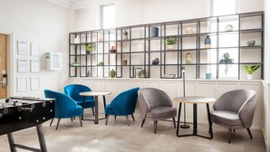 A modern lounge area with a foosball table, blue and grey chairs, and a black shelving unit with various decorative items. - Holiday Inn Leeds Wakefield M1 Jct.40 by IHG (Ossett)