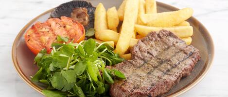 A plate with steak, fries, a tomato slice, and greens.
