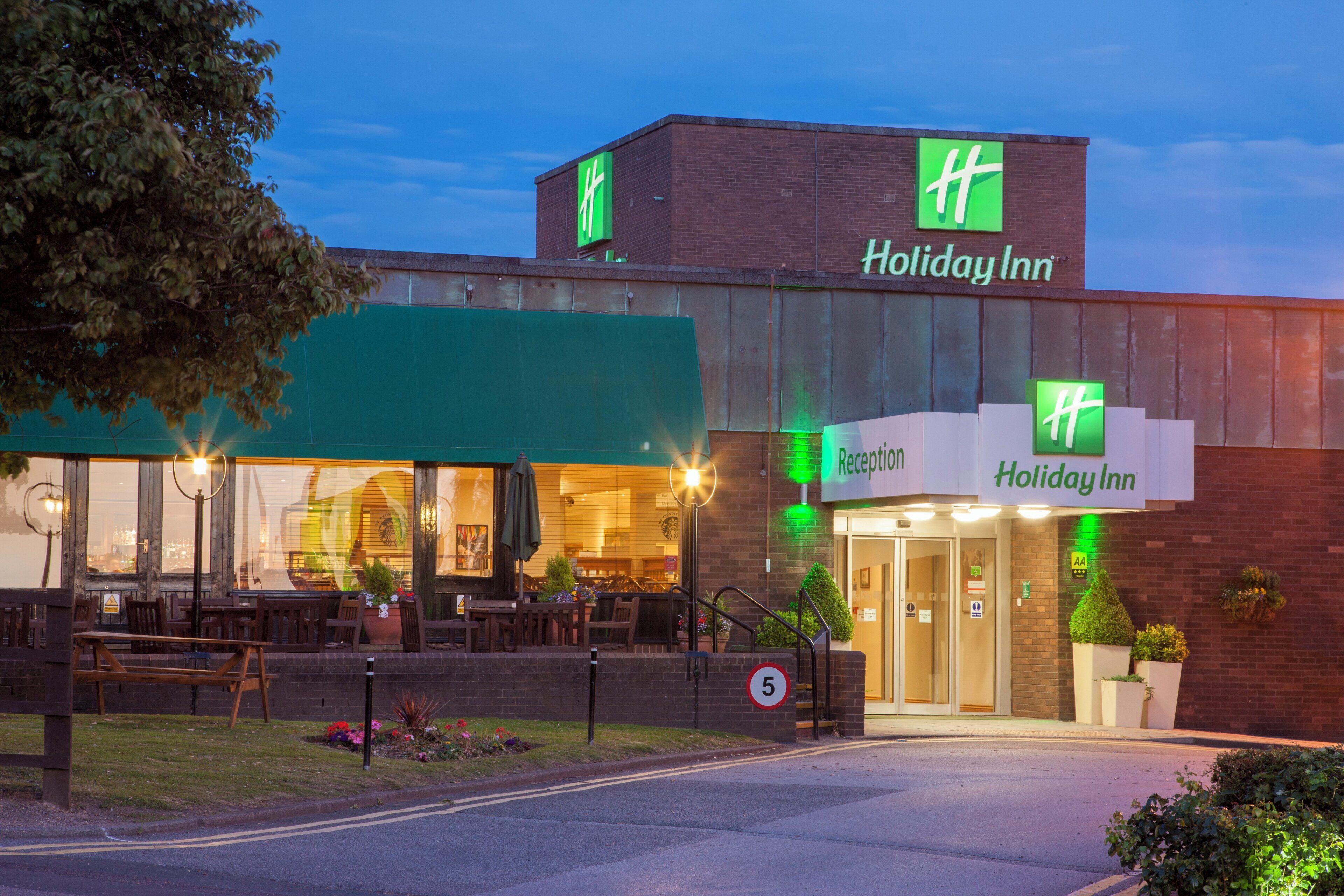 Un hotel Holiday Inn con zona de recepción, asientos exteriores y fachada de ladrillo.