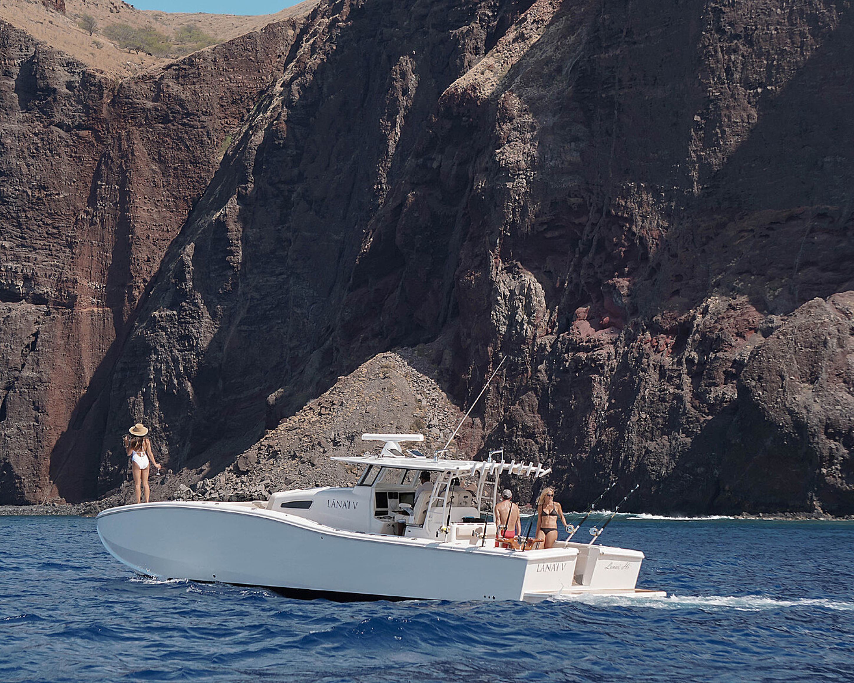 A white boat with the name "LANAVIV" on the side, sailing on blue water with a rocky cliff in the background.