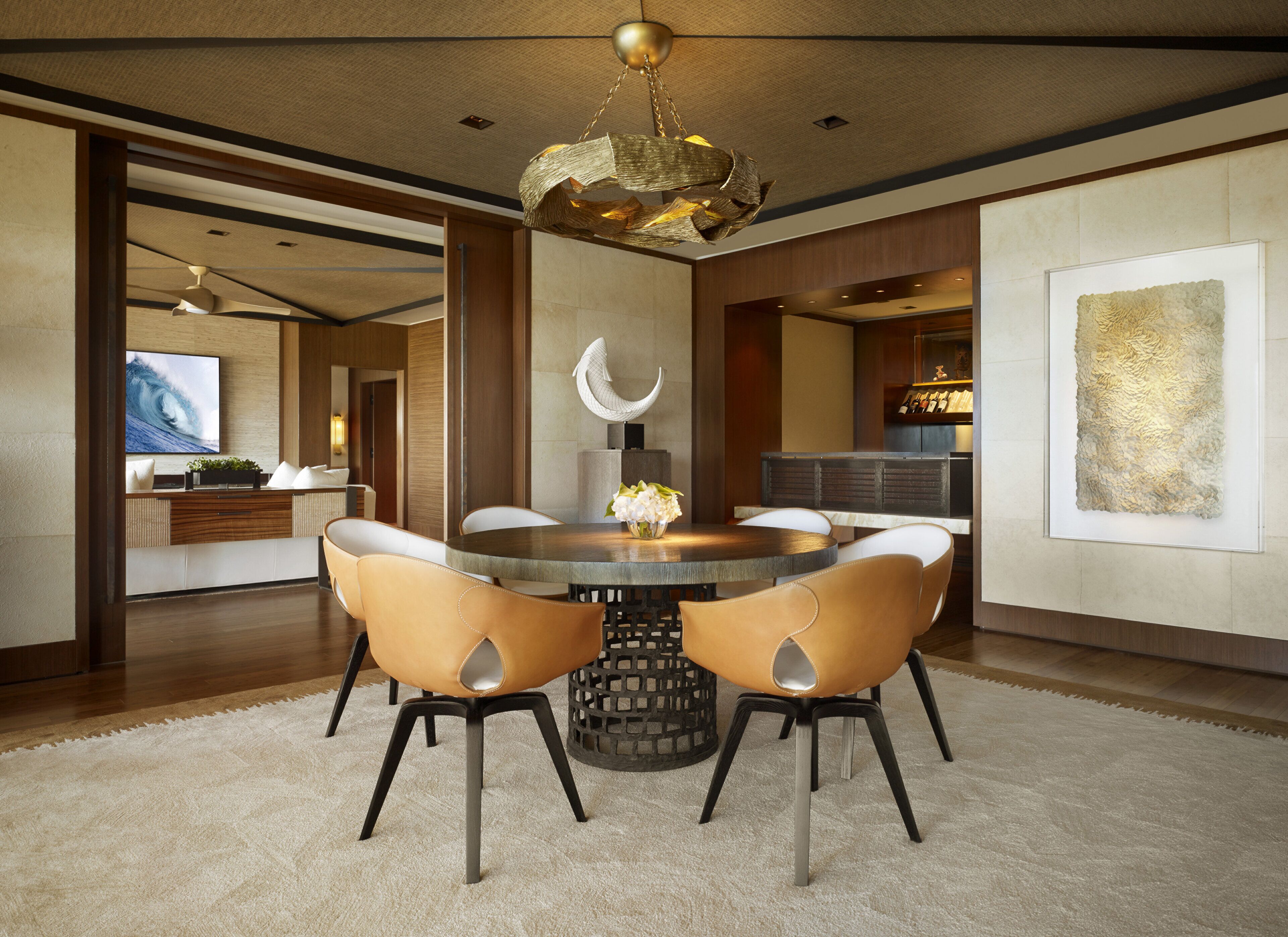 A modern dining area with a round table, leather chairs, a chandelier, and a large artwork on the wall.