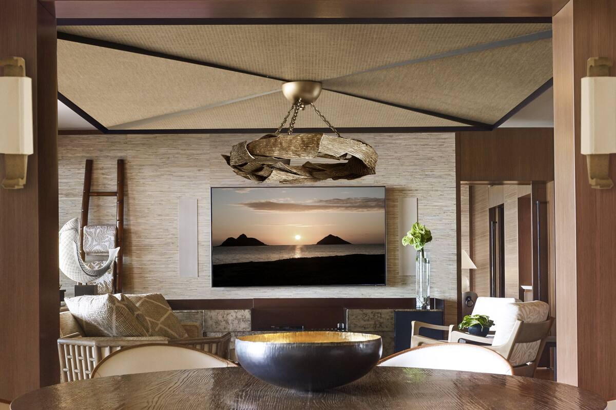 Ein modernes Wohnzimmer mit großem Flachbildfernseher an einer strukturierten Wand, einem Holzesstisch mit Stühlen und einer außergewöhnlichen Pendelleuchte.