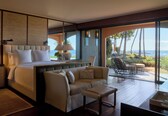A modern bedroom with a large bed, bedside lamps, a sofa, and a view of the ocean.