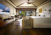 A modern hotel room with a large TV, a bed, a sofa, and a view of the ocean.