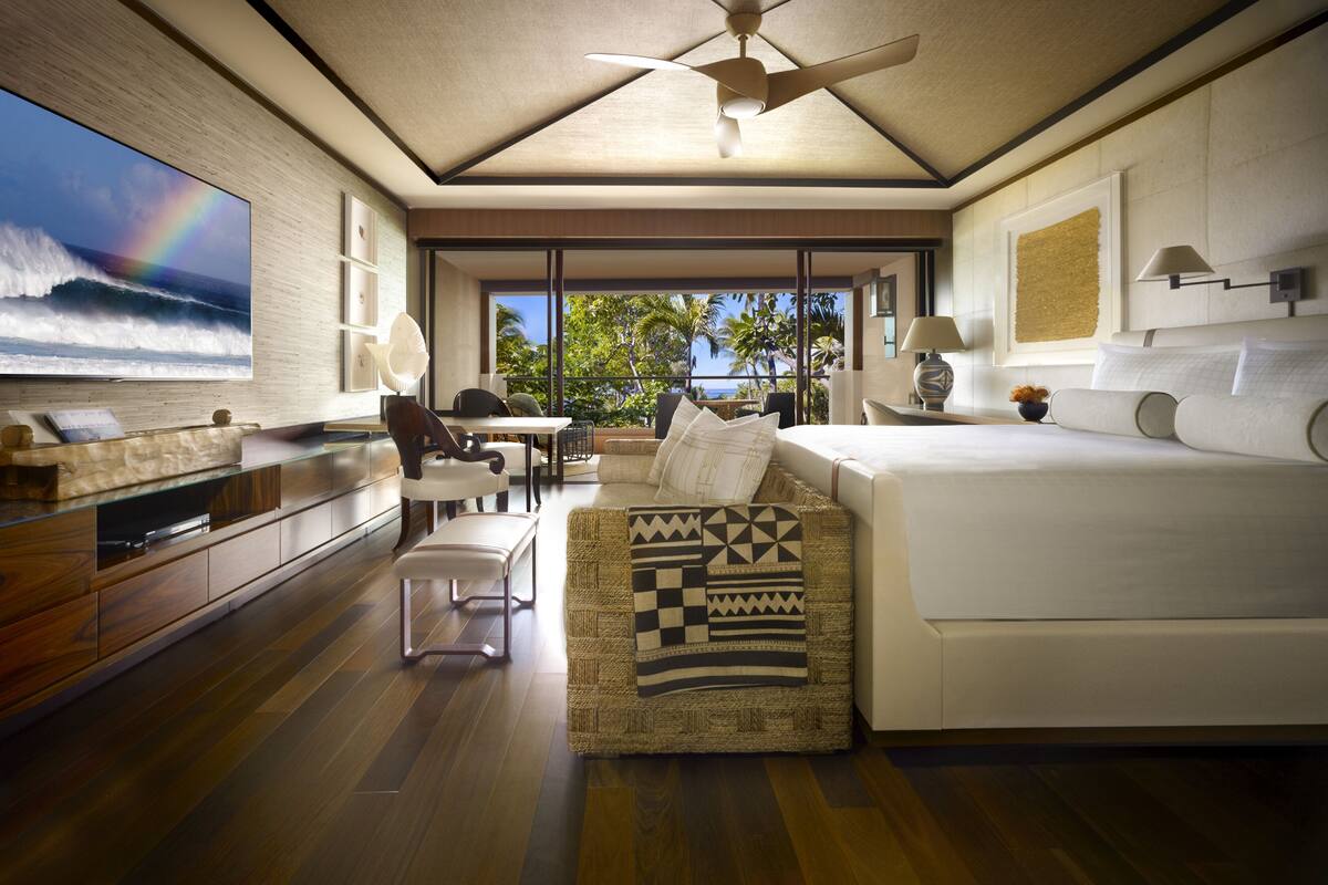Ein modernes Hotelzimmer mit großem Fernseher, einem Bett, einer Couch und Blick aufs Meer.