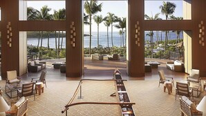 A spacious lounge with a long wooden table, comfortable seating, and large windows offering a view of the ocean and palm trees. - Four Seasons Resort Lanai (Lanai City)