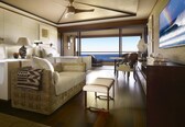 A spacious room with a large bed, a sofa, a dining area, and a view of the ocean.