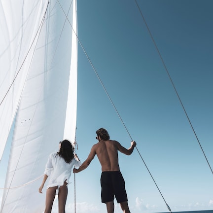 A sailboat with two people on deck, a clear sky, and calm sea.