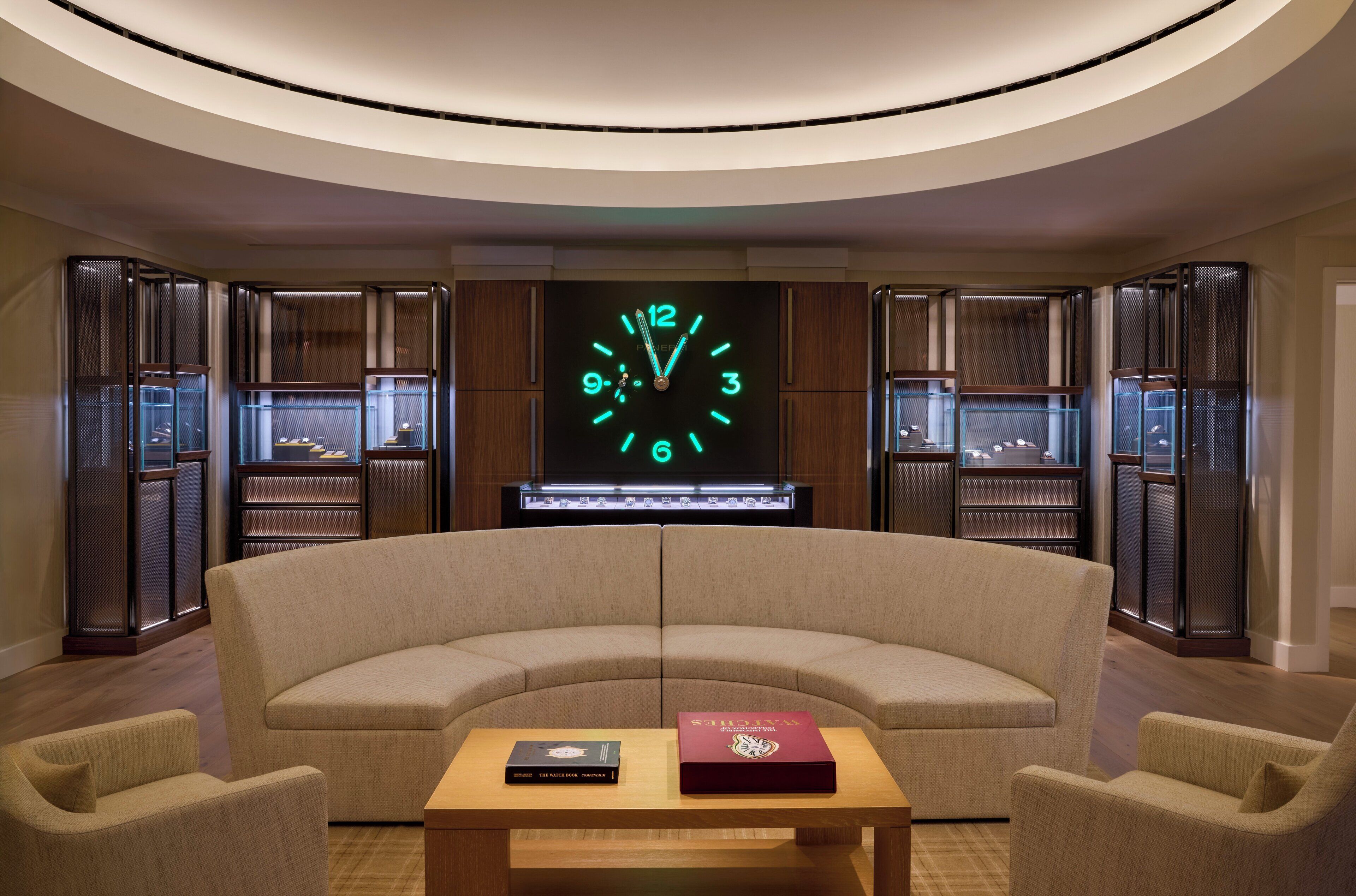 A modern lounge area with a curved sofa, a wooden coffee table, and a large wall clock.