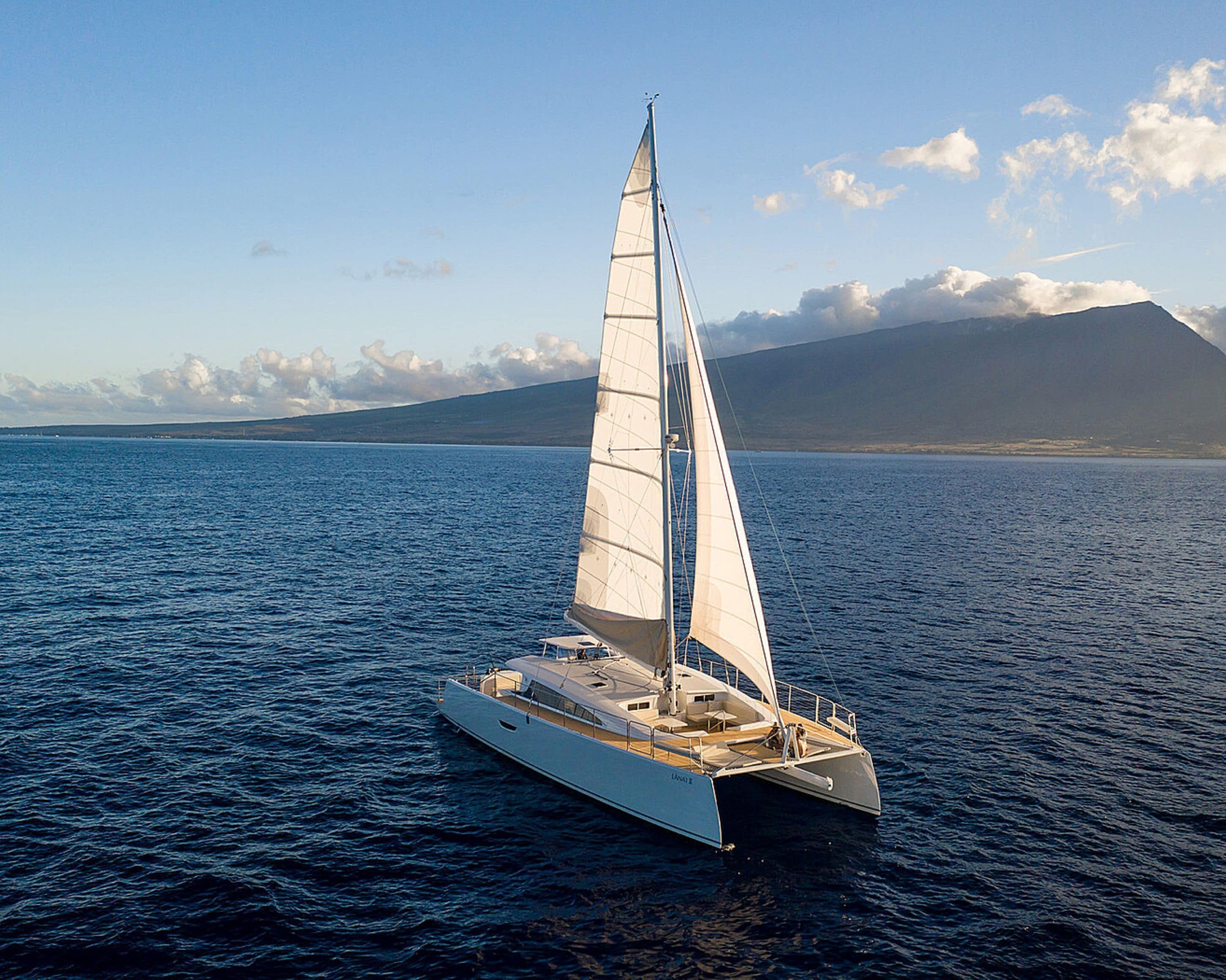 A sailboat on a calm sea with a mountainous backdrop.