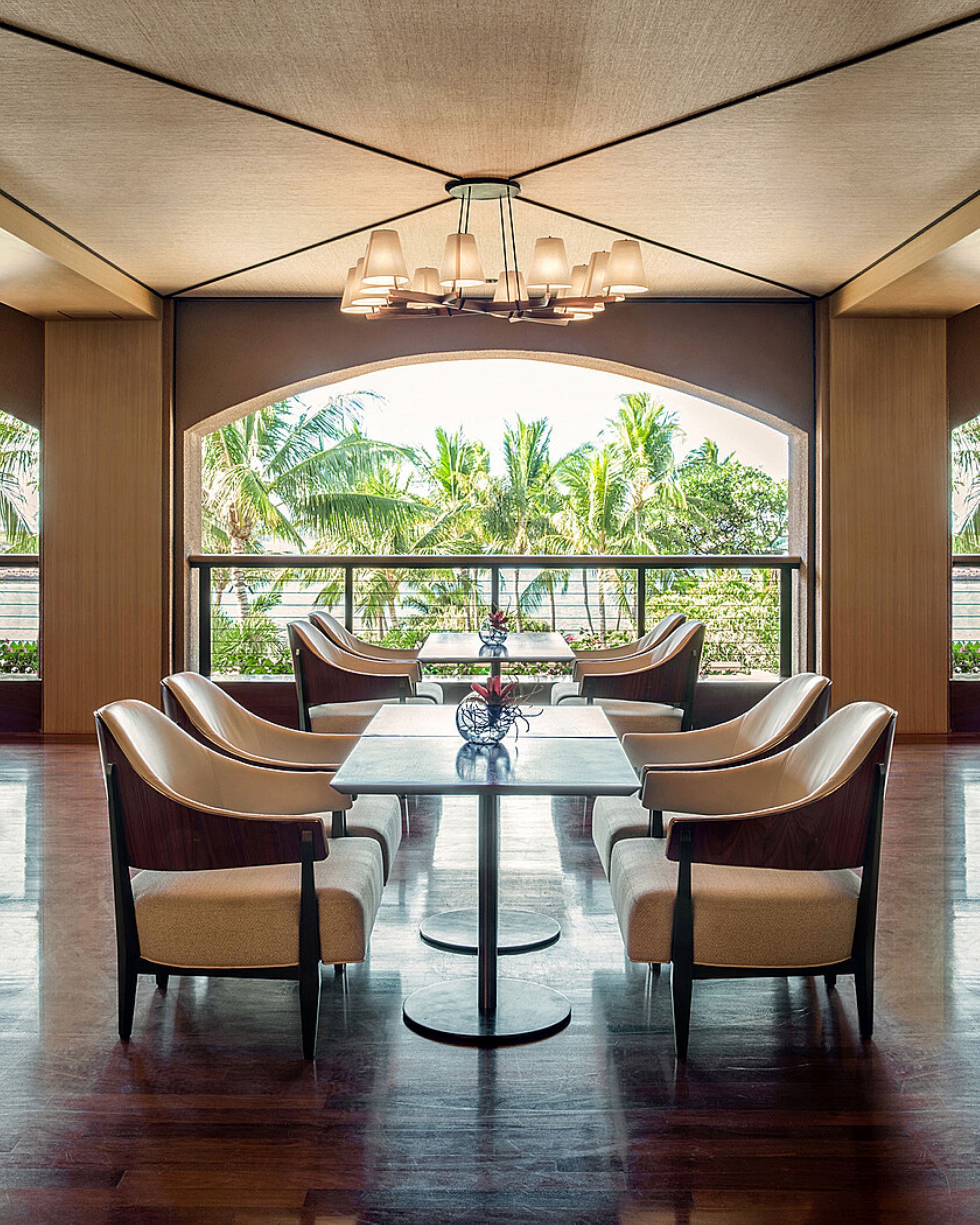 A spacious dining area with a high ceiling and large windows offering a view of palm trees.