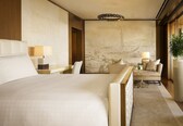 A hotel room with a large bed, a seating area with a sofa and armchairs, a dining table, and a mural on the wall.