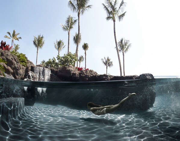 A person swimming in a pool with a waterfall and palm trees in the background. - Four Seasons Resort Lanai (Lanai City)