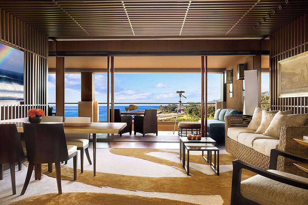 Ein modernes Wohnzimmer mit einem großen Fenster mit Blick auf den Ozean, ausgestattet mit einer Couch, Sesseln und einem Couchtisch.
