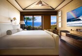 A spacious bedroom with a large bed, a ceiling fan, a view of the ocean, and a dining area with a view.