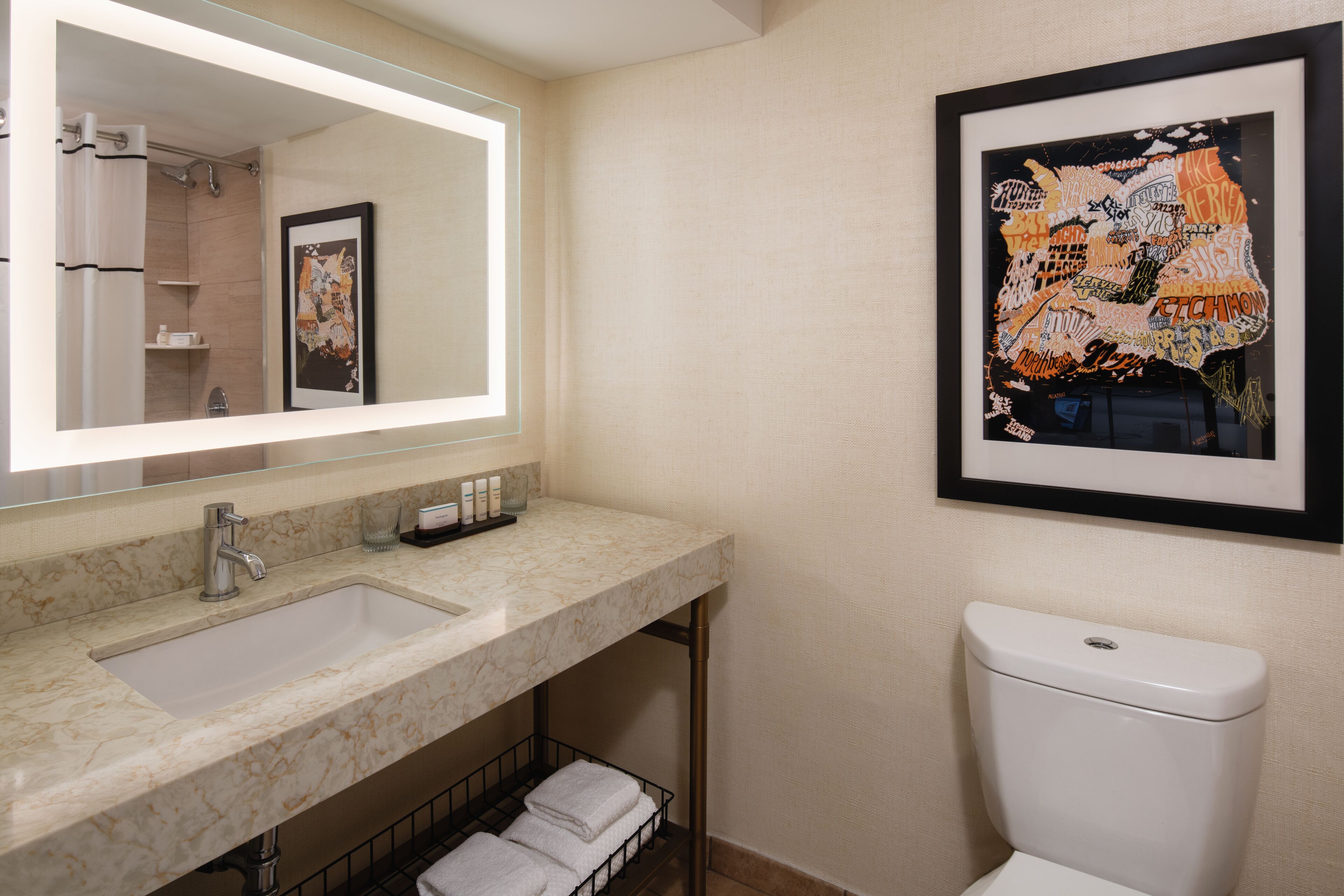Une salle de bain avec un lavabo en marbre, une œuvre d’art encadrée au mur et des toilettes.