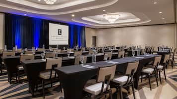 A conference room with multiple tables and chairs, a large screen displaying a presentation, and a carpeted floor.