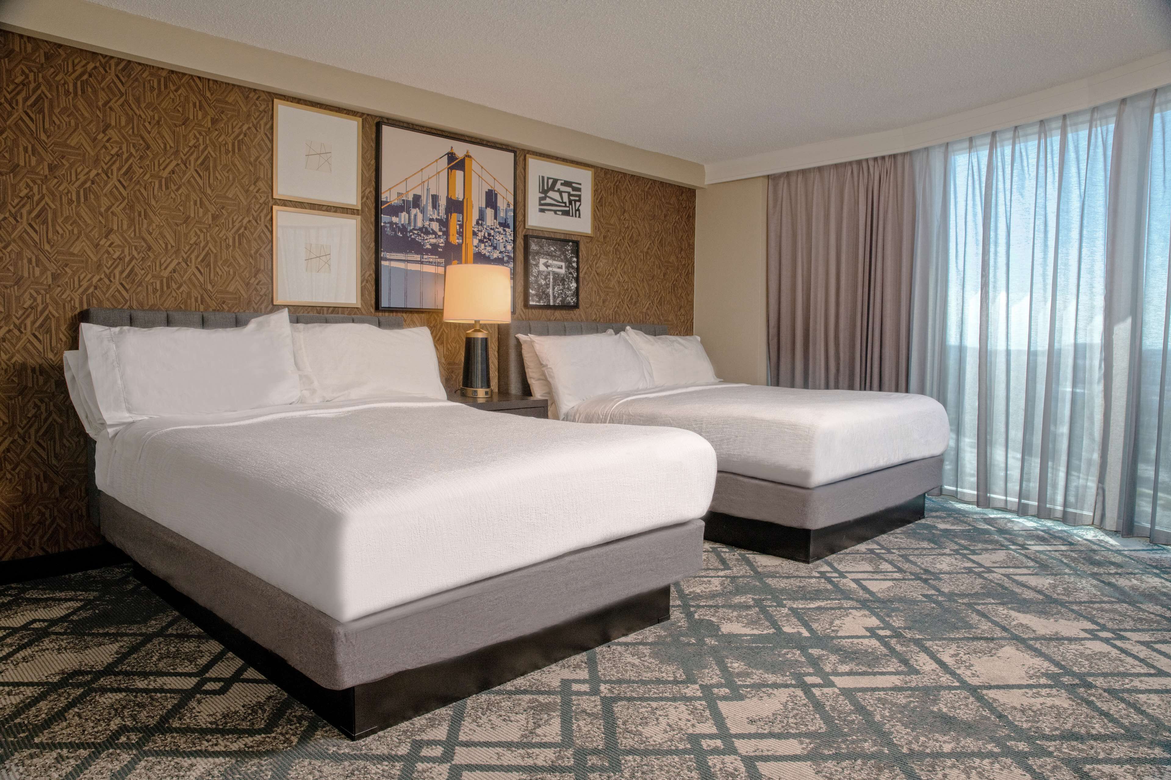 A hotel room with two beds, a patterned carpet, and framed artwork on the wall.