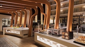 A modern hotel lobby with a buffet area featuring a variety of food items and a coffee station.