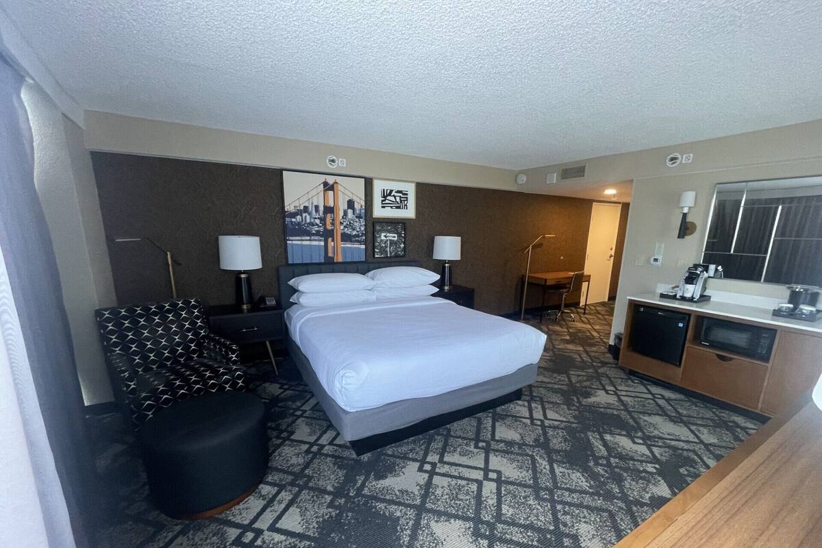 Een hotelkamer met een groot bed, een bureau, een stoel, een klein tafeltje en een spiegel.