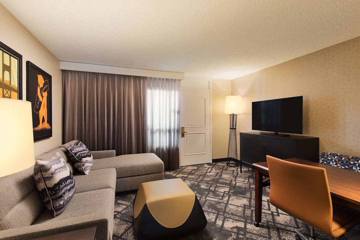 Een hotelkamer met een bank, voetenbankje, eettafel en televisie.