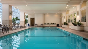 A large indoor swimming pool with clear water, surrounded by lounge chairs and potted plants.