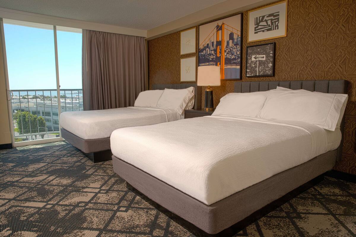 Een hotelkamer met twee bedden, een groot raam met uitzicht en een kamerbreed tapijt met dessin.