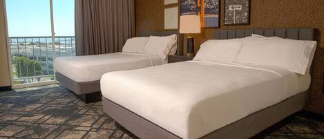 A hotel room with two beds, a large window with a view, and a patterned carpet.