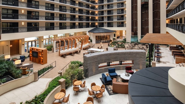 A multi-level hotel atrium with outdoor seating areas, a pool, and a central lounge.