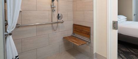 A shower with a bench, a towel rack, and a door leading to a bedroom.