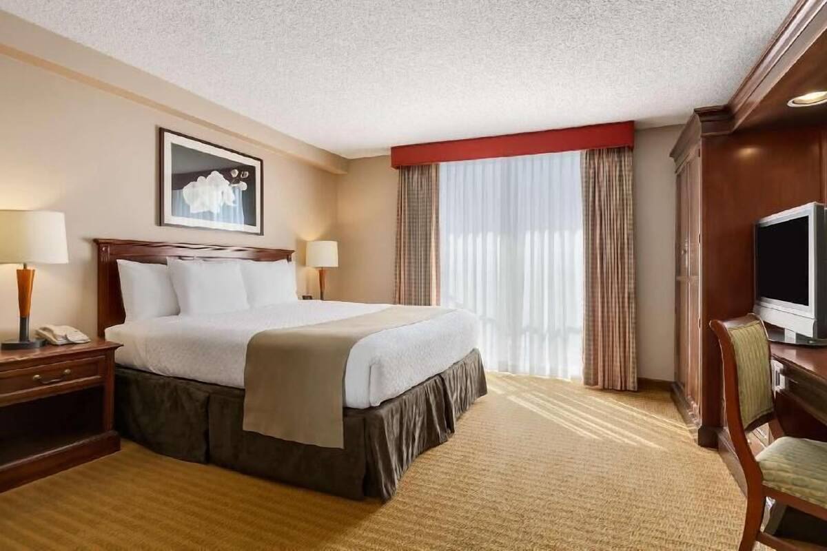 Een hotelkamer met een groot bed, twee nachtkastjes met lampen, een televisie en een raam met gordijnen.