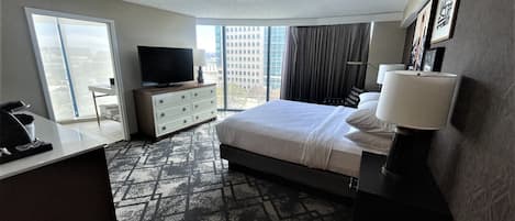 Ein Hotelzimmer mit Bett, Fernseher, Schreibtisch, Kommode und Blick auf die Stadt.
