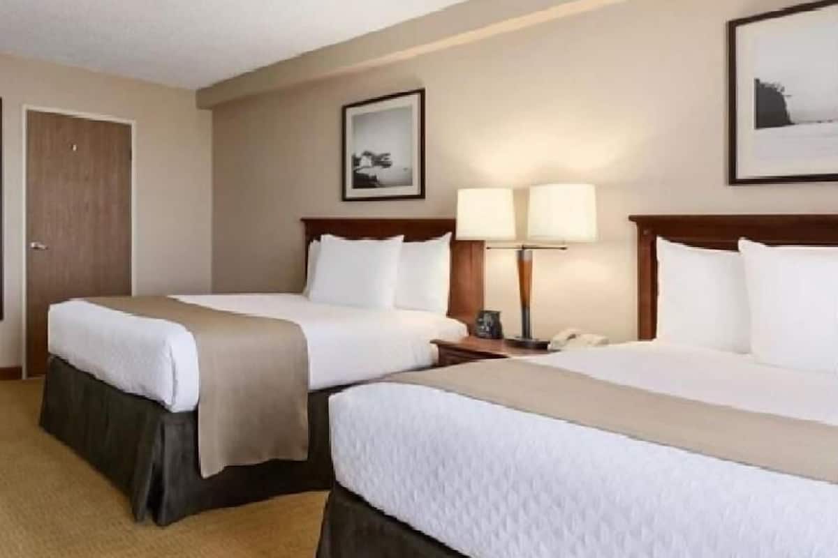Een hotelkamer met twee bedden, een houten hoofdbord, een nachtkastje met een lamp en een ingelijst beeld aan de muur.