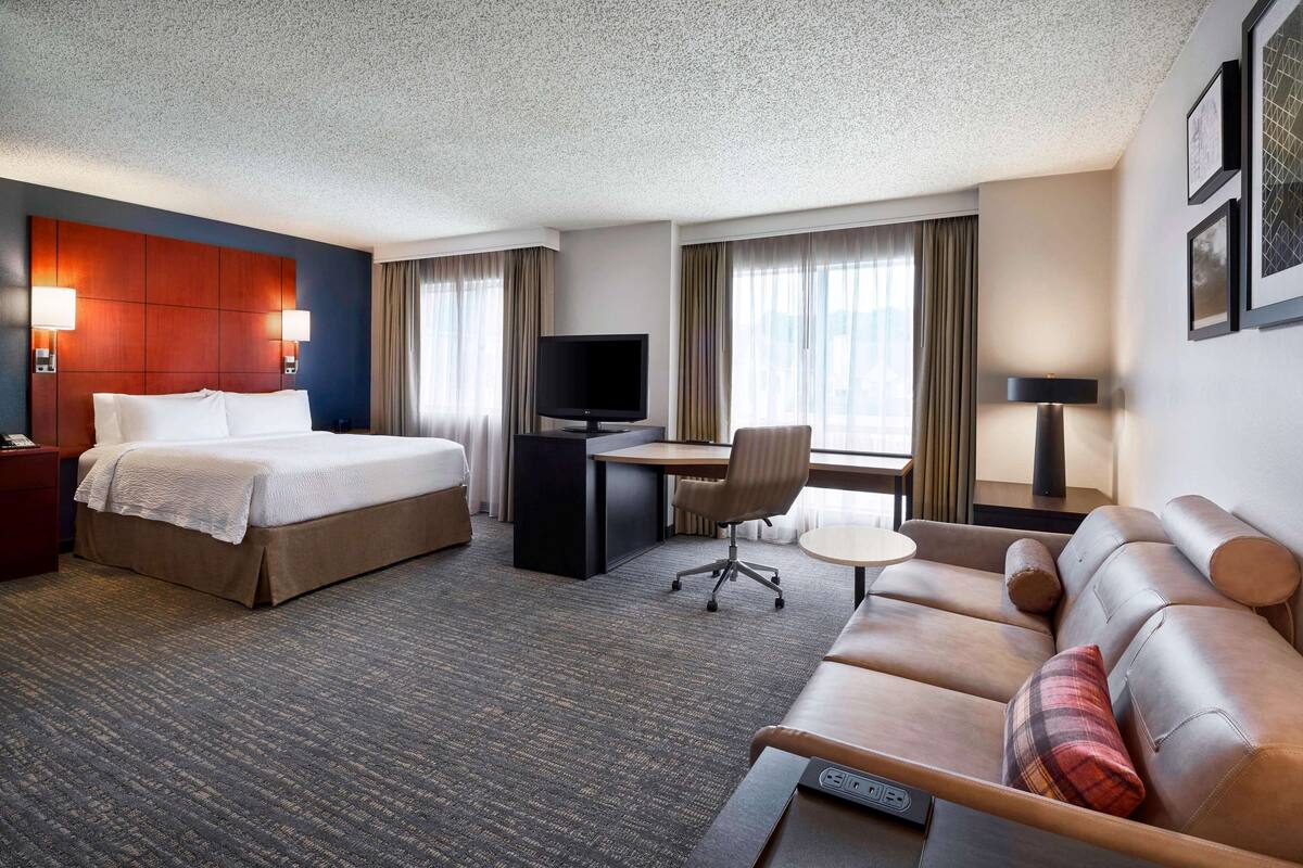 A hotel room with a bed, desk, TV, and seating area.