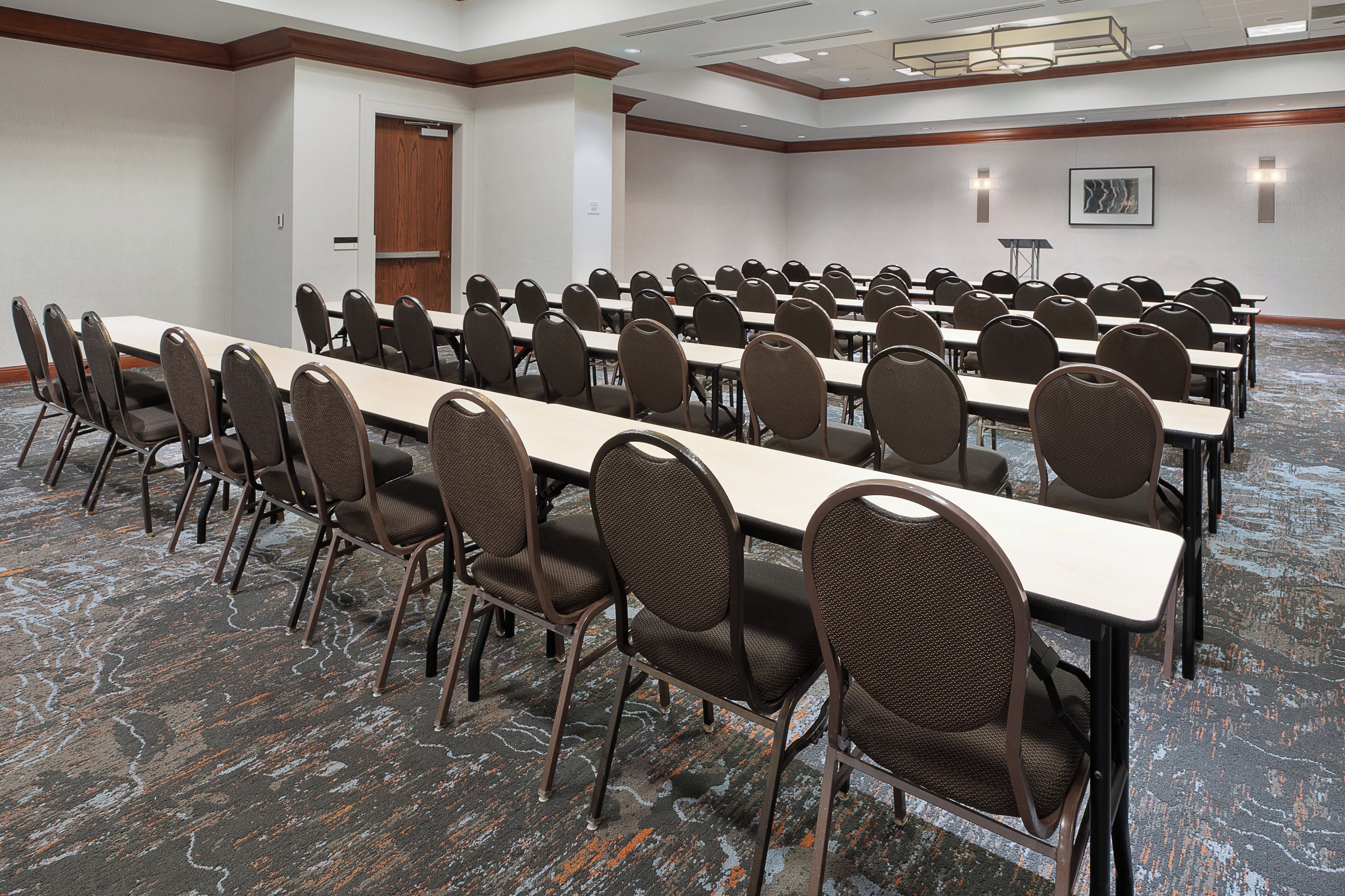A conference room with rows of tables and chairs, a door, and a wall-mounted light fixture.
