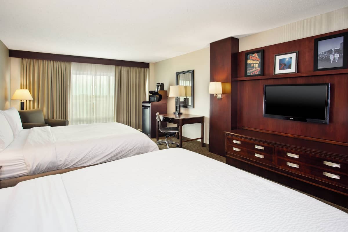 A hotel room with two beds, a desk, a chair, a TV, and a minibar.