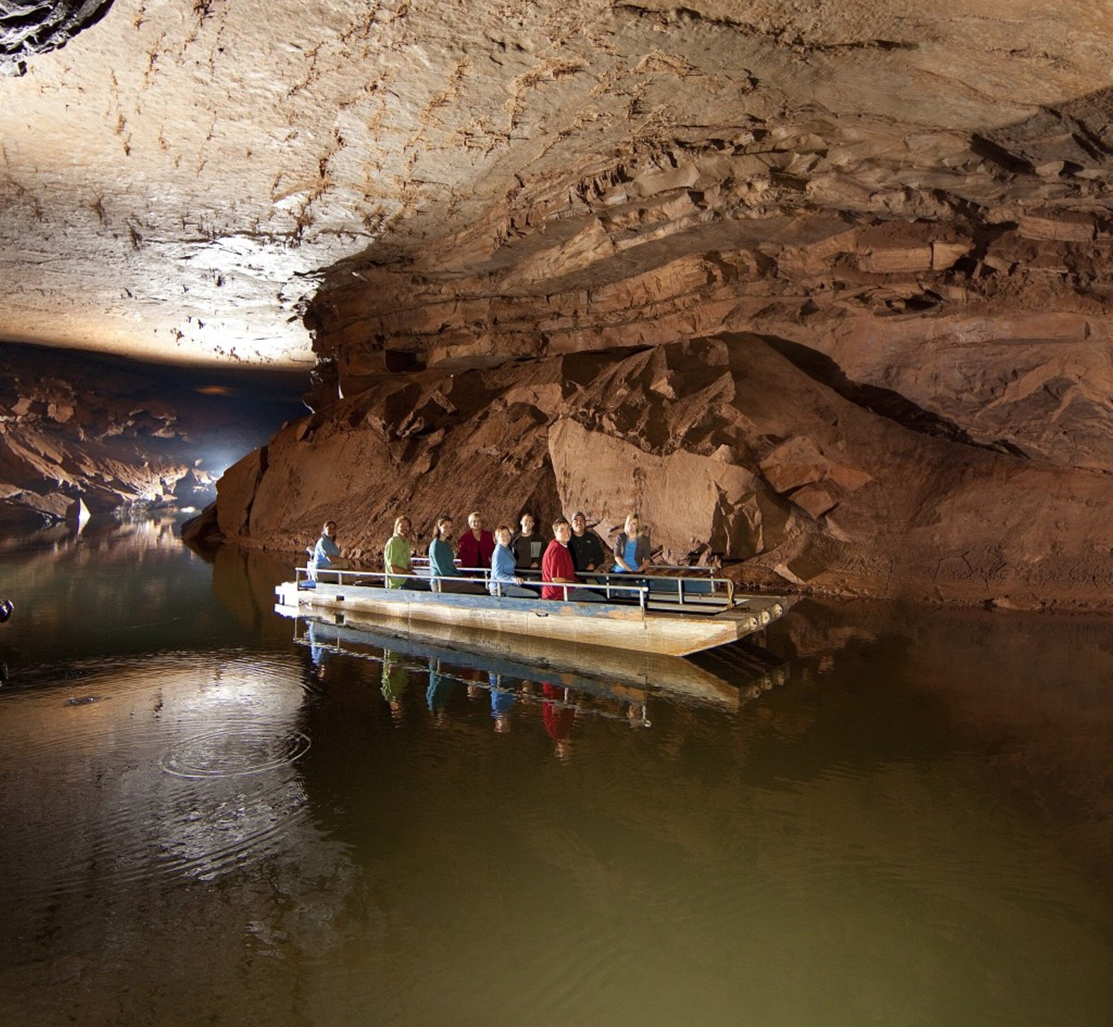 A group of people on a boat inside a cave with water at the bottom.