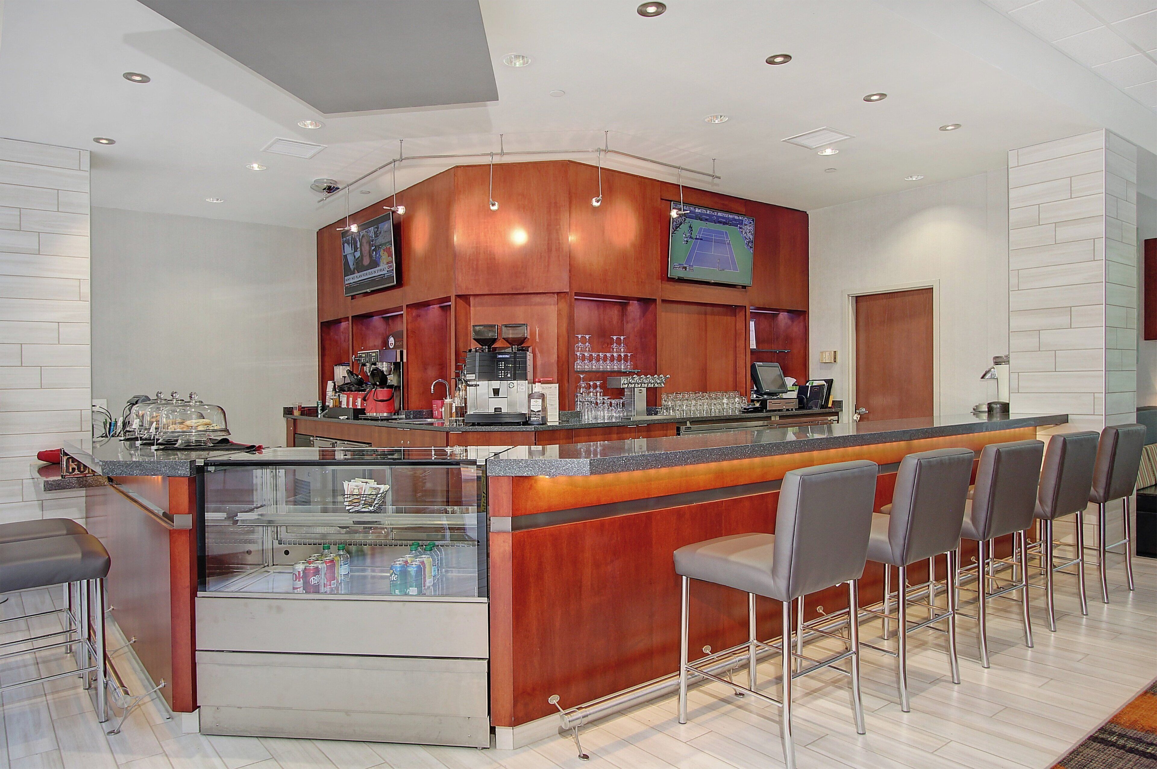 A modern bar area with a wooden counter, multiple seating options, and a television screen.