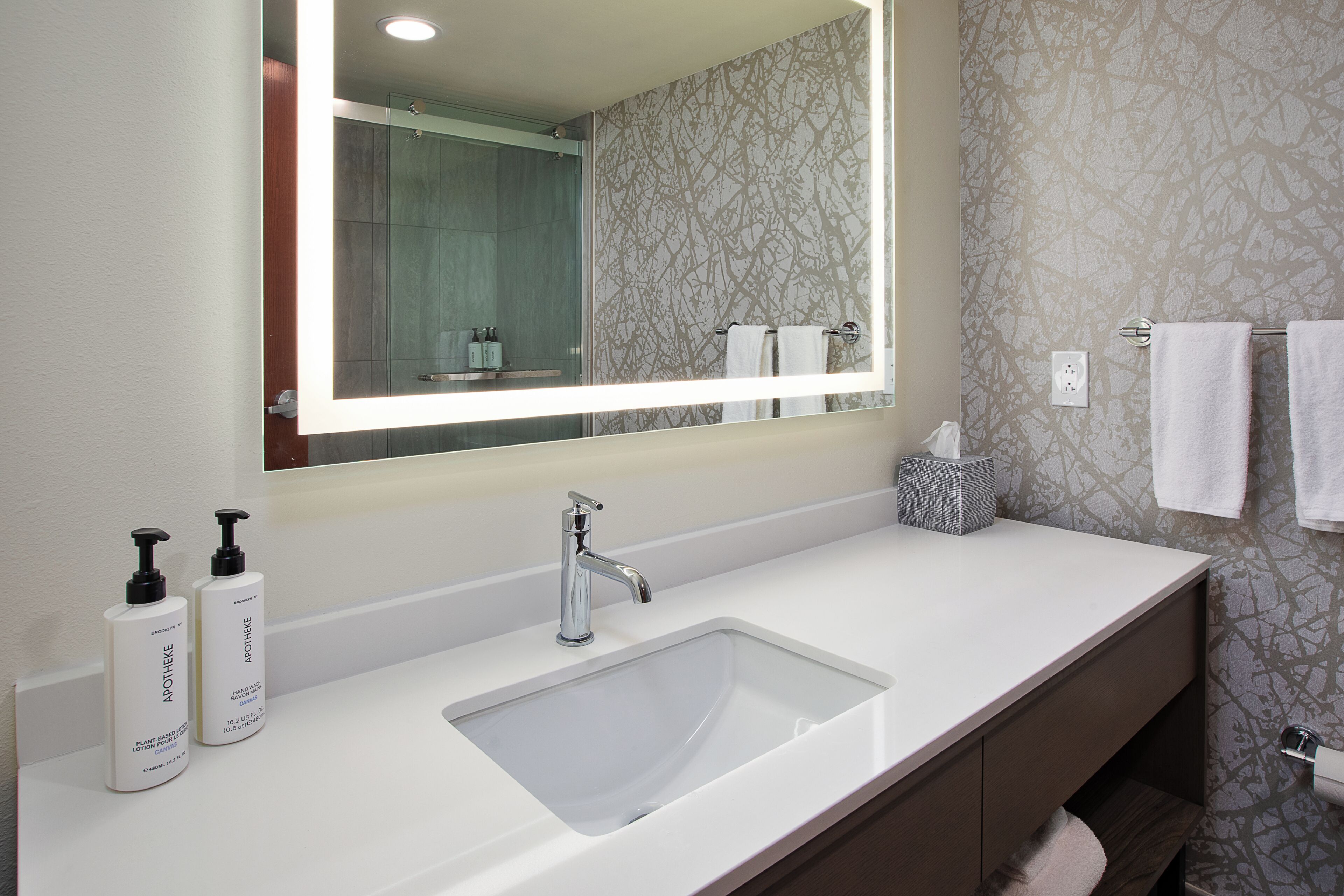 Une salle de bain avec un grand miroir, un lavabo blanc et deux flacons de savon liquide pour les mains.