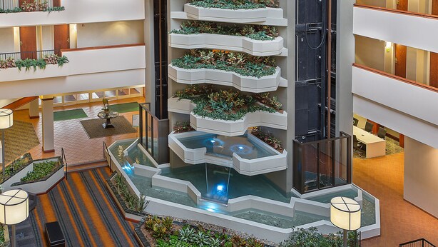 A multi-level atrium with a central water feature, surrounded by planters with greenery. - Holiday Inn University Plaza-Bowling Green by IHG (Bowling Green)