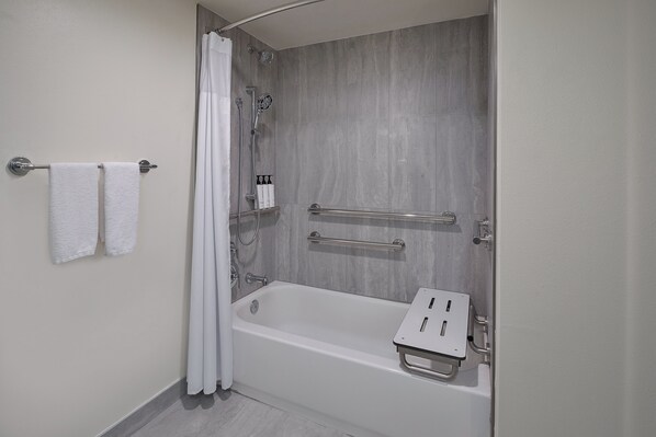 A modern bathroom with a bathtub, shower, and handrails.