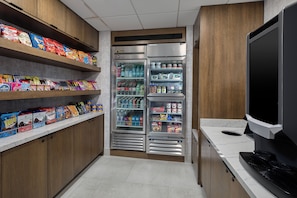 Un pasillo estrecho con estantes llenos de refrigerios y un refrigerador para bebidas.